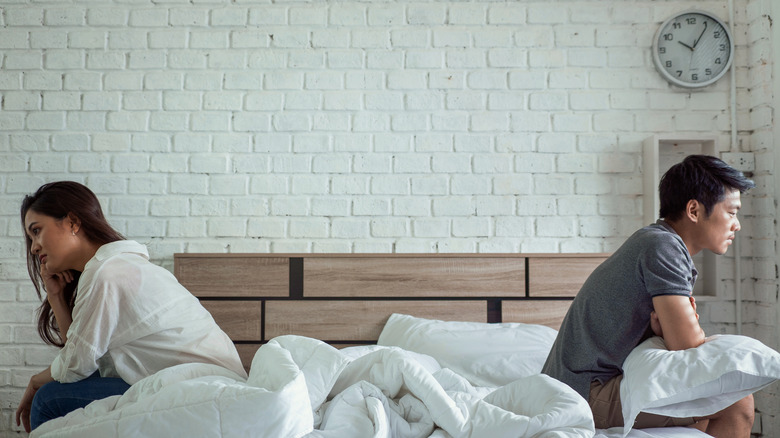 couple sitting apart on bed