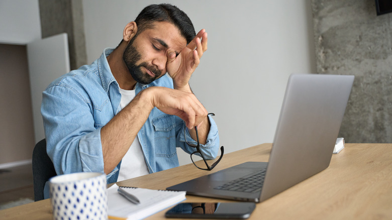 man rubbing eyes at desk