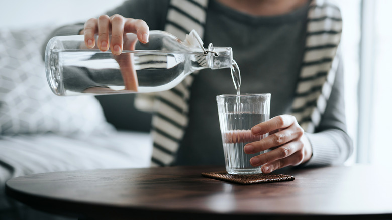 A woman's hands pouring water from a bottle into a glass