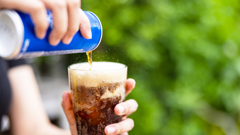 A woman's hands pouring a can of soda into a glass