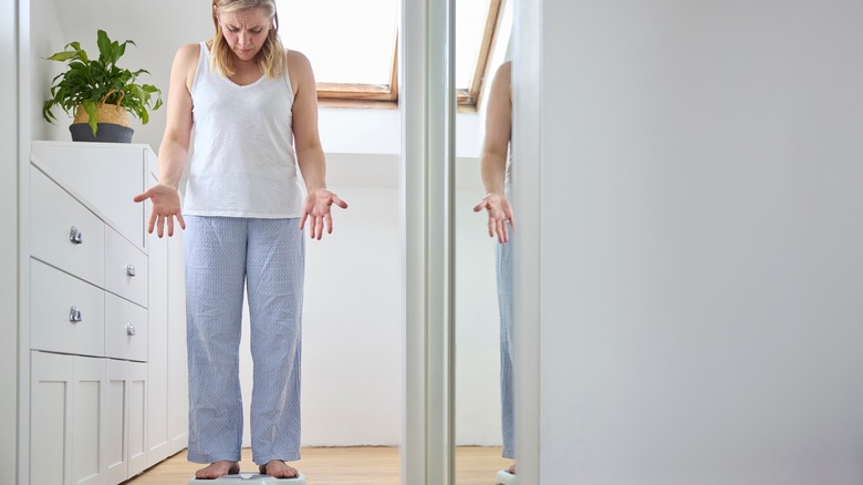 Woman standing on scale, shocked at weight gain
