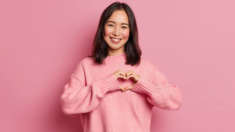 young woman smiling with heart-shaped fingers