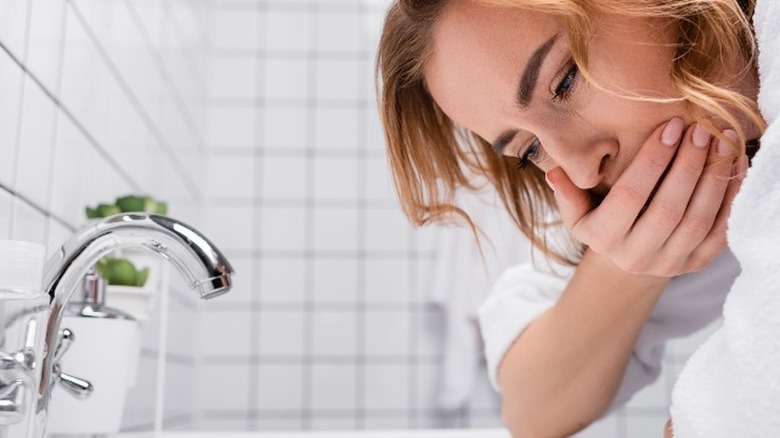 Nauseous woman standing over sink