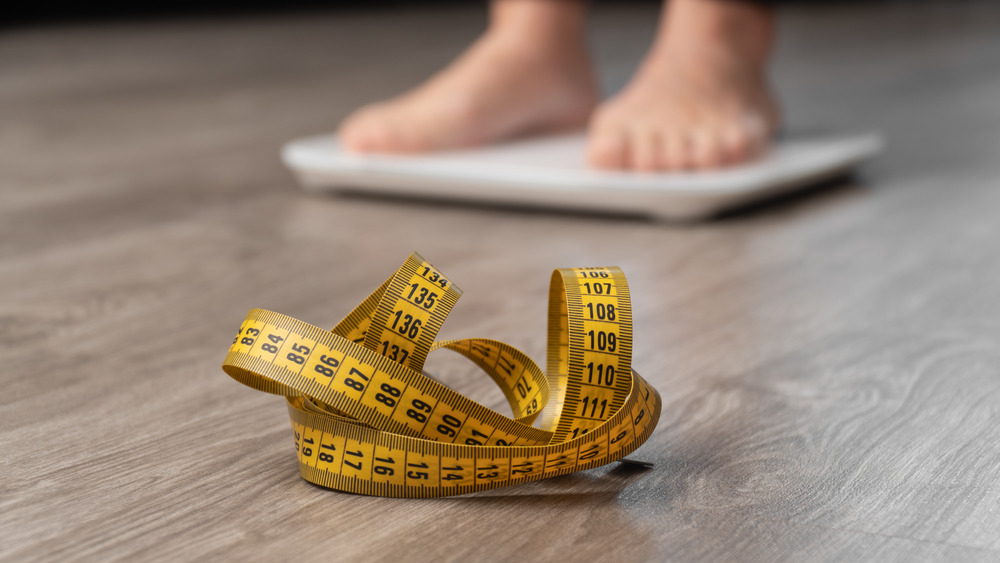 person on scales with tape measure