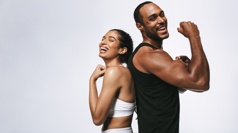 man and woman standing next to one another the man has big muscles 