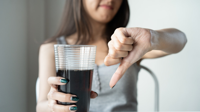 woman holding soda giving thumbs down