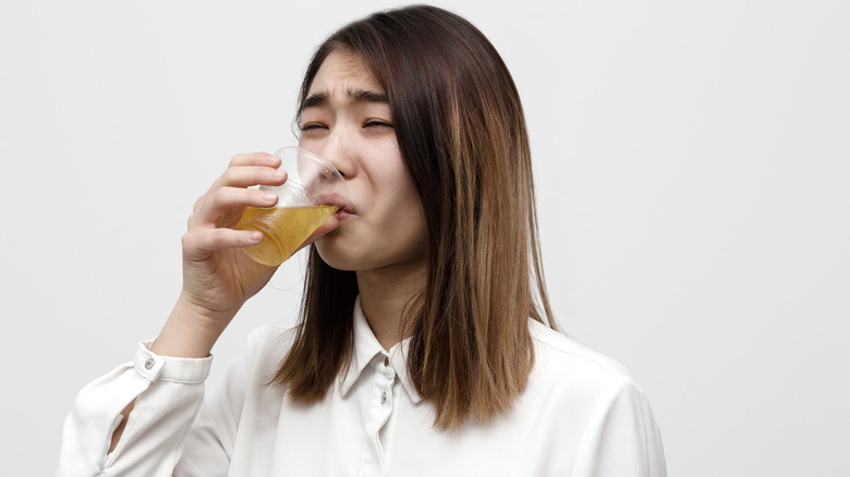 young woman looking disgusted drinking yellow drink