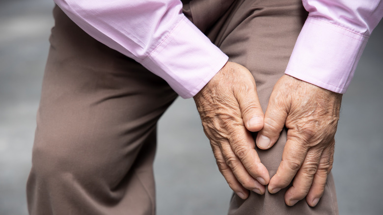 an elderly man holding his knee in pain 