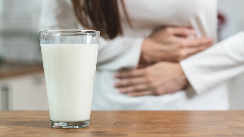 Woman holding stomach by a glass of milk