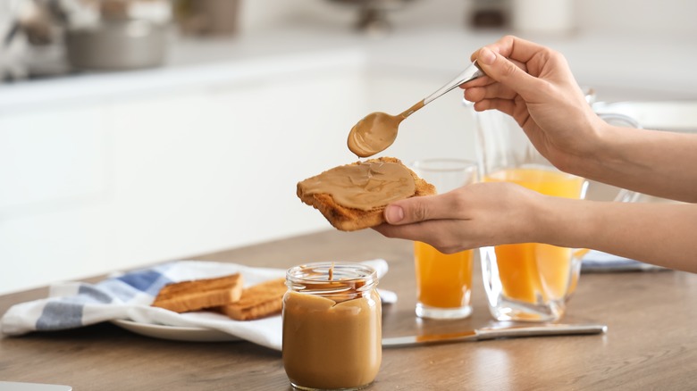 woman's hands spreading peanut butter onto toast