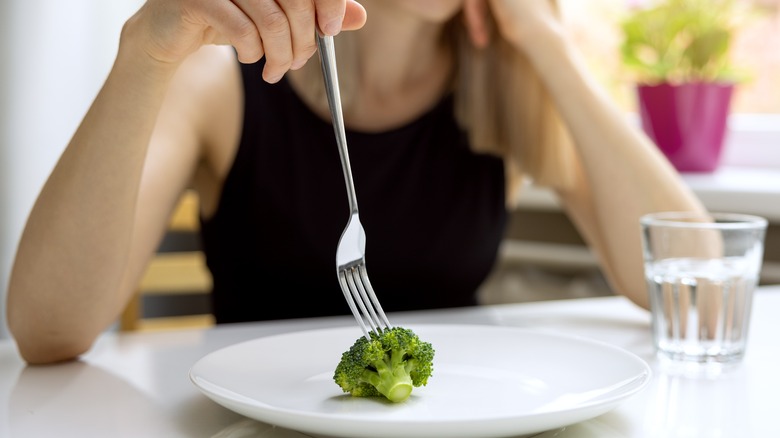 woman playing with broccoli on plate
