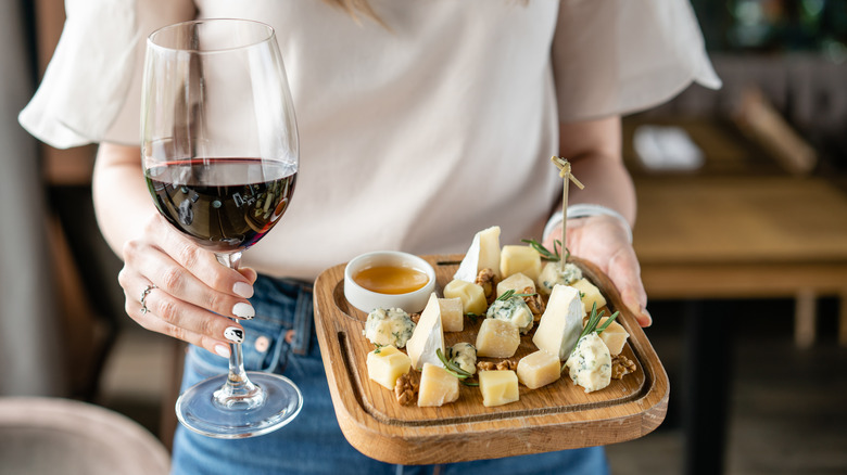 woman holding cheese board and glass of red wine