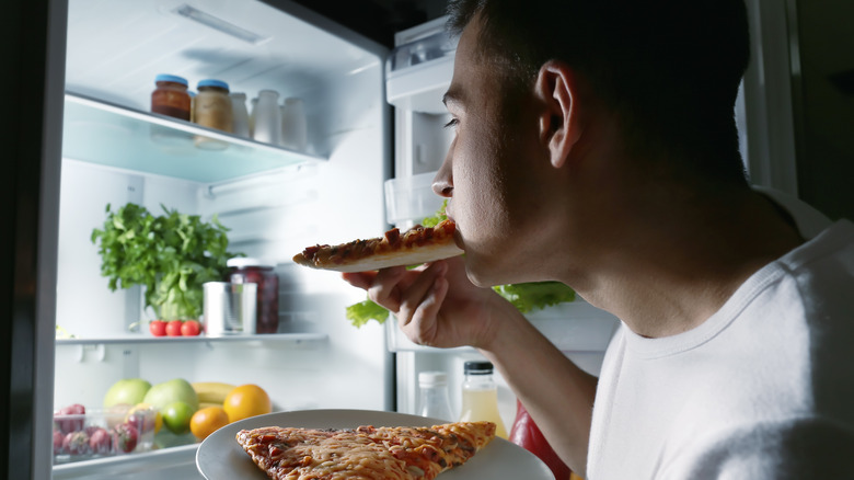 man eating pizza out of fridge at night