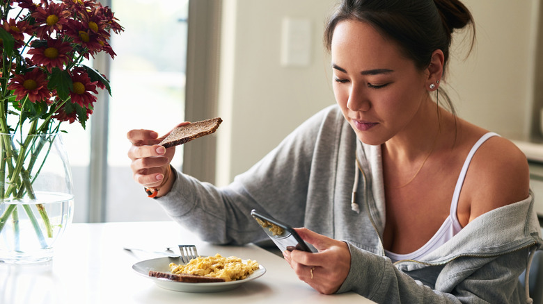 young woman eating plate of scrambled eggs and toast