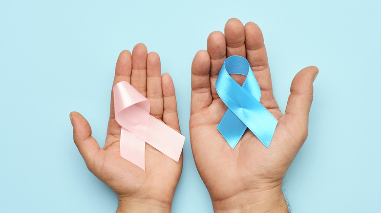 woman's hand holding pink breast cancer ribbon and man's hand holding blue prostate cancer ribbon