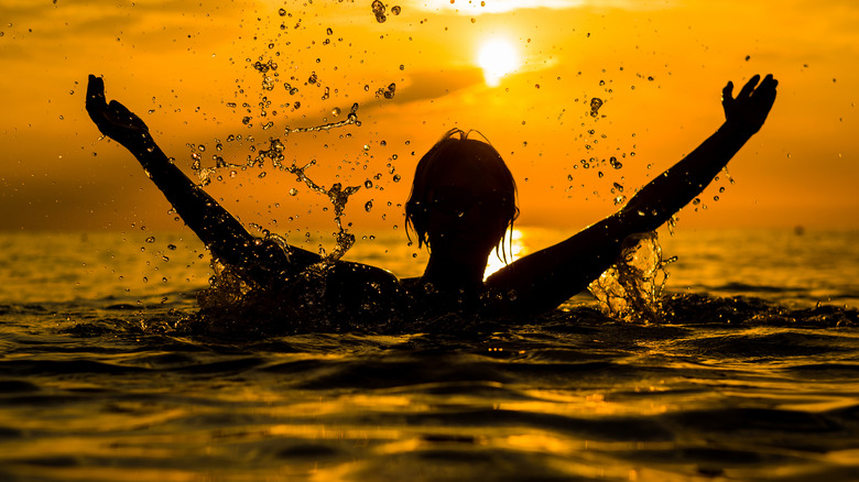 Silhouette of person in the ocean with arms raised against the sunset