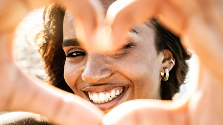 close up of smiling woman making heart gesture