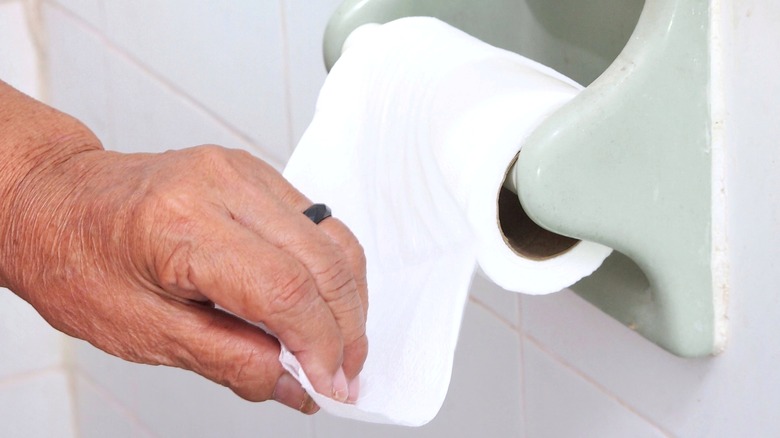 older female hand pulling toilet paper 