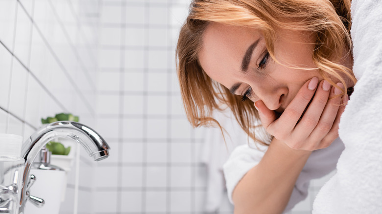 female covering mouth leaning over sink