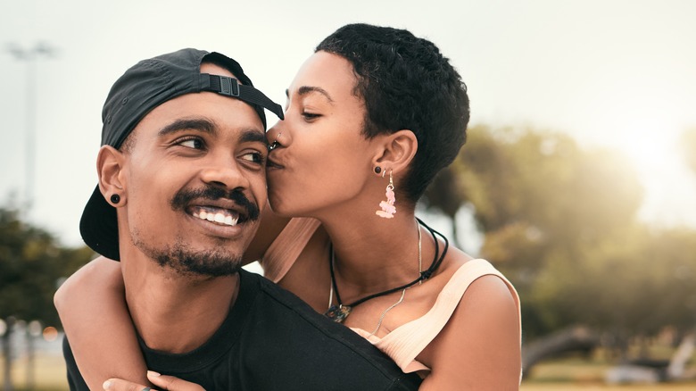 A woman embracing a man from behind and kissing his cheek