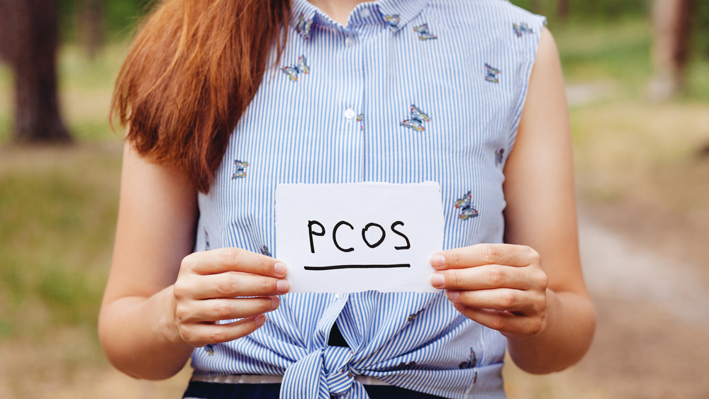 woman holding piece of paper with PCOS on it