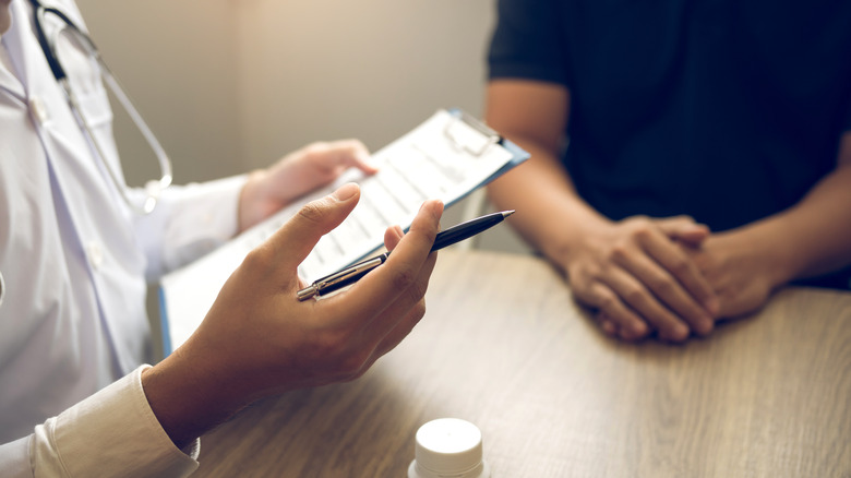 Closeup view of doctor holding clipboard and speaking to patient