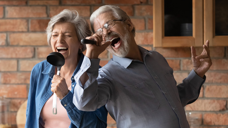 Elderly couple playfully singing into kitchen utensils