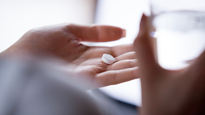 Close-up over a woman's shoulder as she holds a pill in her hand