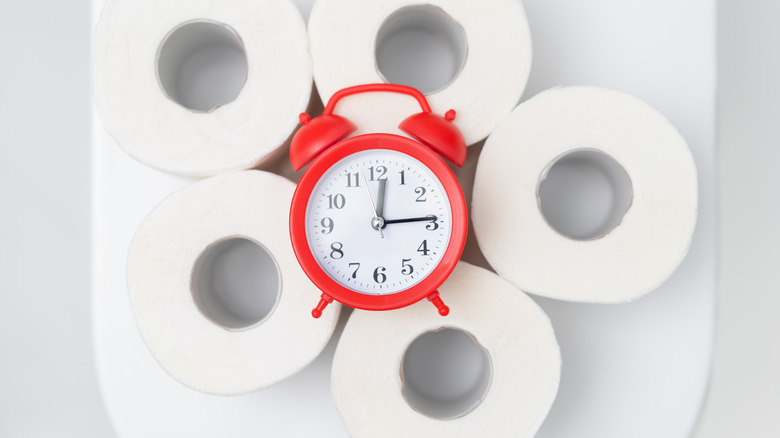 red clock atop rolls of toilet paper