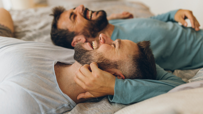 two men smile while cuddling in bed