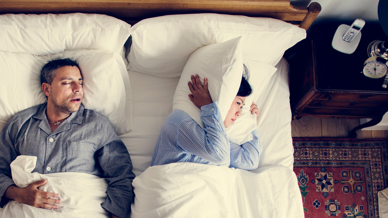 Man snoring next to frustrated woman in bed