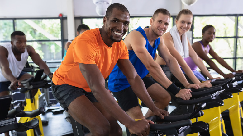 four people smiling and looking at the camera while in a spin class