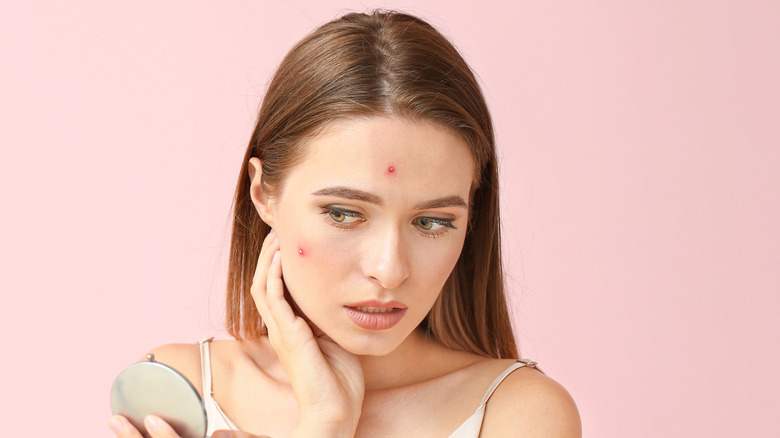 Woman with acne looking with concern at her reflection in the mirror