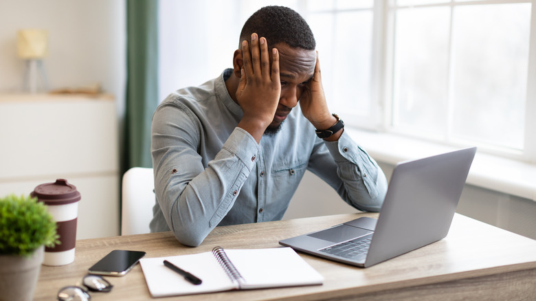 Man sitting at his laptop, holding his head because he's stressed