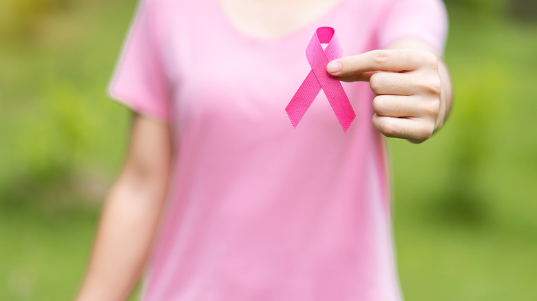 Woman in a pink shirt holding up a breast cancer awareness ribbon