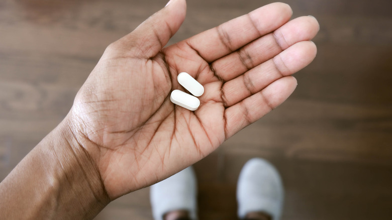 A woman's hand holding two small caplets of medicine