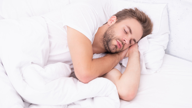 A man sleeping in a bed with white sheets and comforter