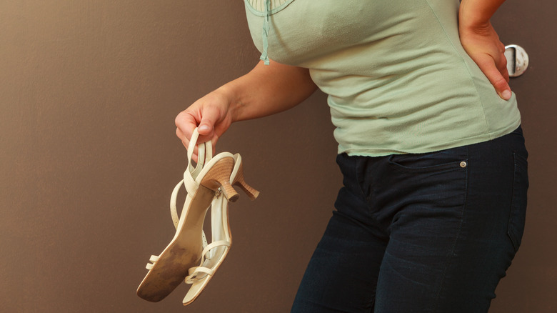 Woman with high heels in hands, holding back in pain