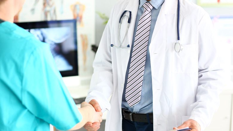 Doctor wearing a long striped tie shaking hands with staff member in scrubs