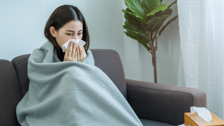 woman wrapped in blanket blowing nose