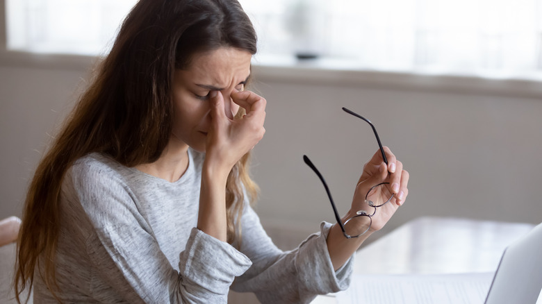 A woman holding her glasses in one hand and pinching her nose in exhaustion