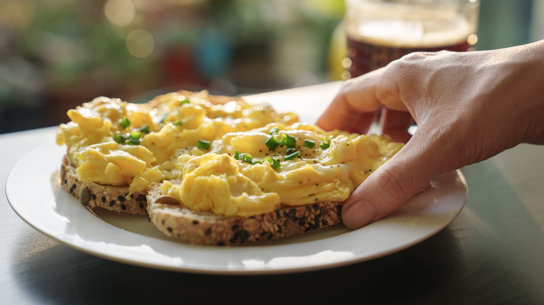 A hand reaching for toast topped with scrambled eggs