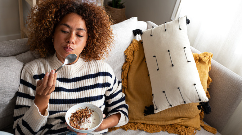 A woman eating yogurt and granola while sitting on her couch