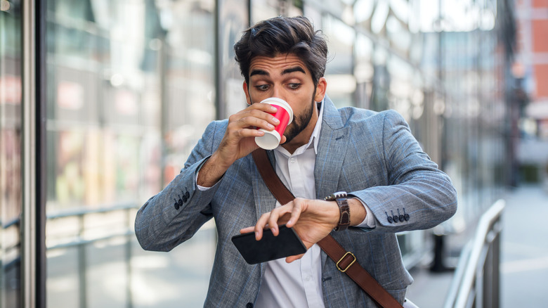 A man looking at his watch while drinking coffee