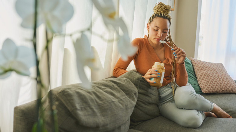 Woman on couch eating peanut butter