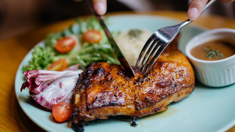 Person slicing grilled chicken on plate