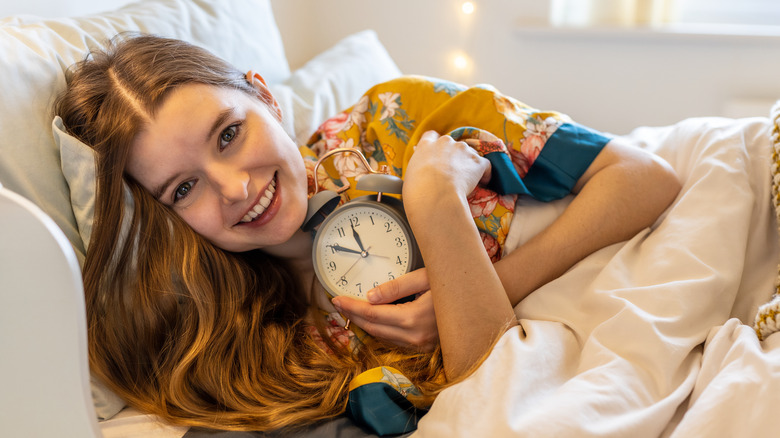 woman in bed smiling while holding a clock