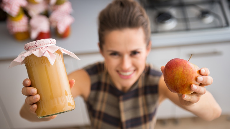 woman holding an apple and a jar of applesauce