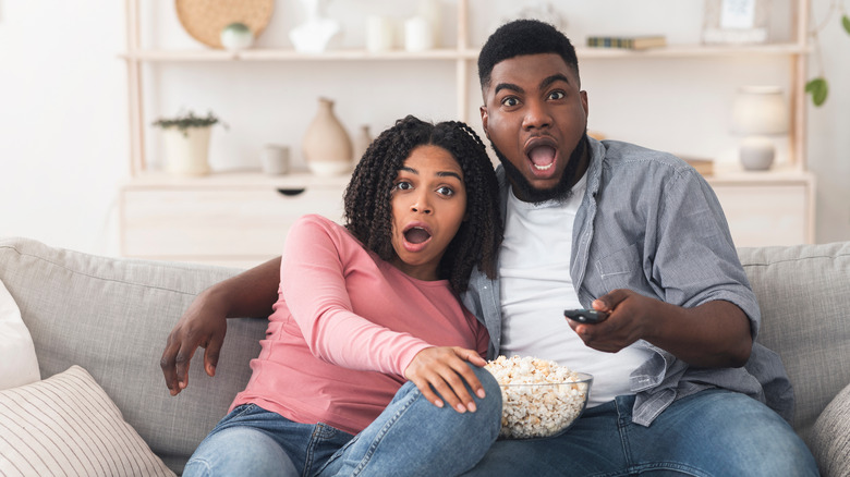 Couple with popcorn watching scary movie at home