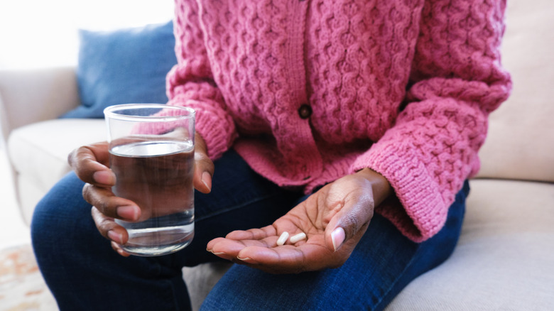 woman on sofa taking medications with glass of water